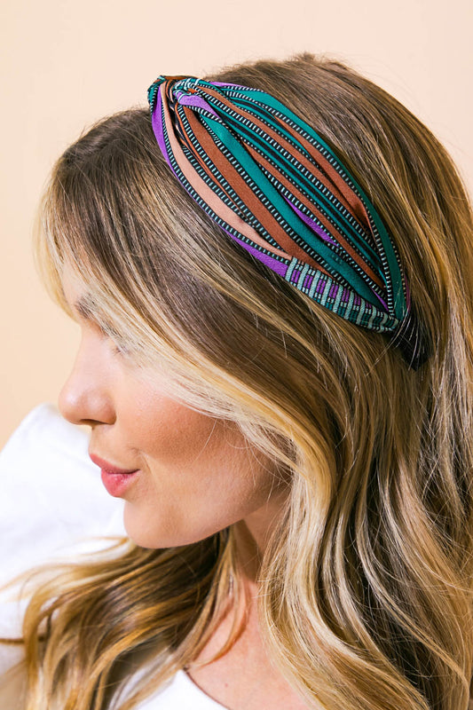 A woman with long, wavy hair wears a colorful, patterned headband. She is facing slightly sideways, giving a soft expression against a neutral beige background.