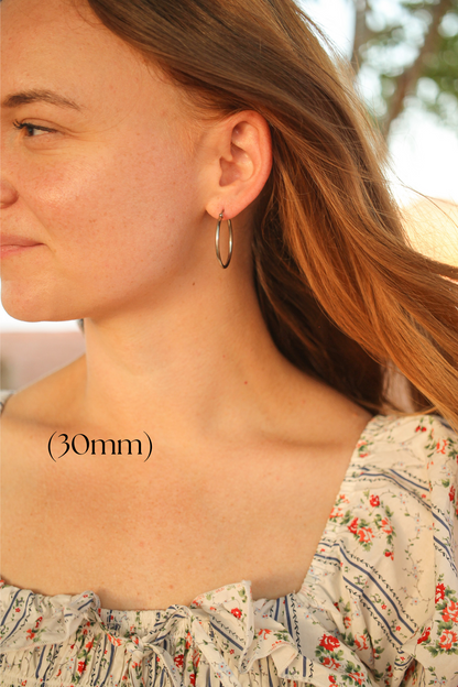 A woman with shoulder-length hair wears a hoop earring, facing slightly to the side. She has a floral-patterned top, and the background suggests an outdoor setting. Text indicates â€œ(30mm).â€