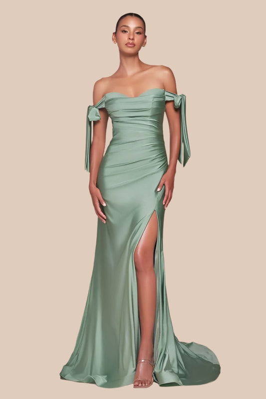 A model stands elegantly in a green, off-the-shoulder gown with side slits and flowing fabric. The backdrop is a soft beige, emphasizing the dress's silhouette and texture.