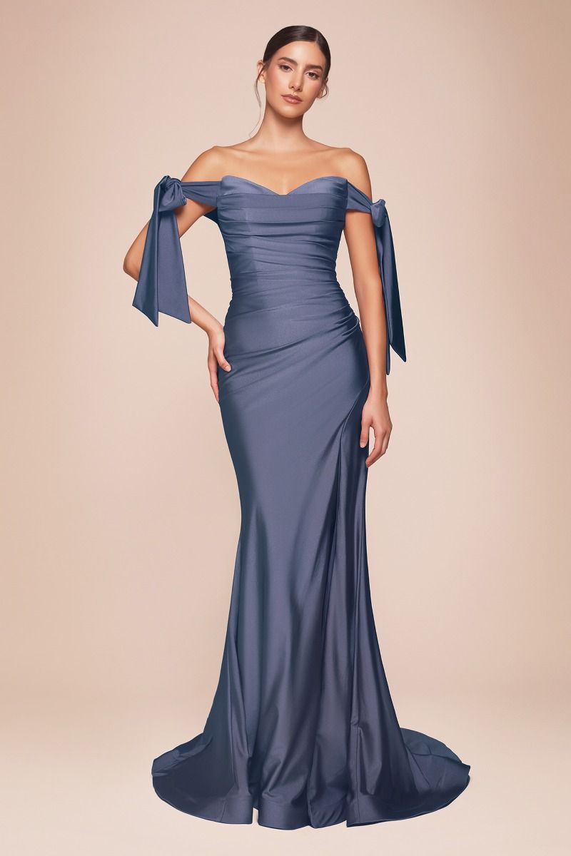 A figure stands elegantly, wearing a fitted, strapless navy gown with off-the-shoulder sleeves tied in bows. The soft, neutral background enhances the gown's sleek design.