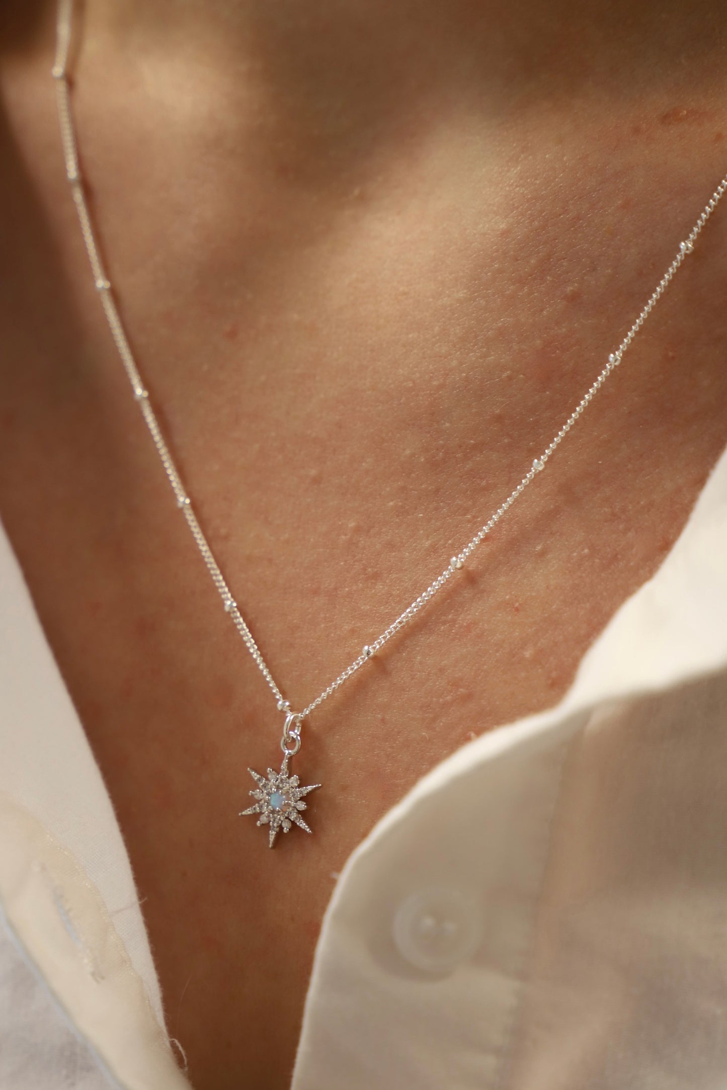 A silver chain necklace adorned with a star-shaped pendant featuring a central gemstone is resting against bare skin, partially visible above a white shirt collar.