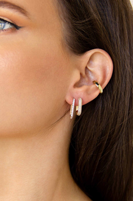 Two sparkling hoop earrings adorn the earlobe of a person, showcasing a close-up of their face against a neutral background, emphasizing the jewelry's shimmer and style.