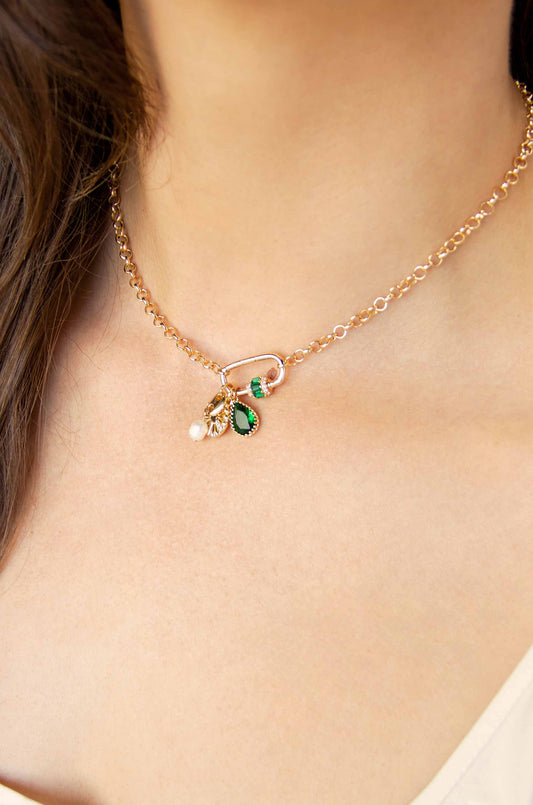 A delicate gold chain necklace adorned with colorful charms, including green and pearl accents, rests on a smooth, light-skinned neck, highlighting a subtle and elegant style.