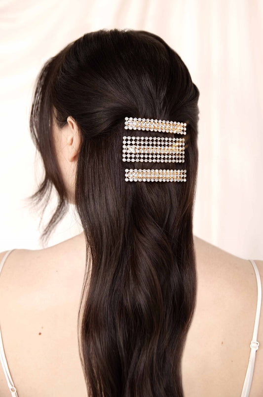 A decorative hair clip adorned with rhinestones holds back long, dark hair, set against a softly blurred light background, emphasizing elegance and style in a feminine context.