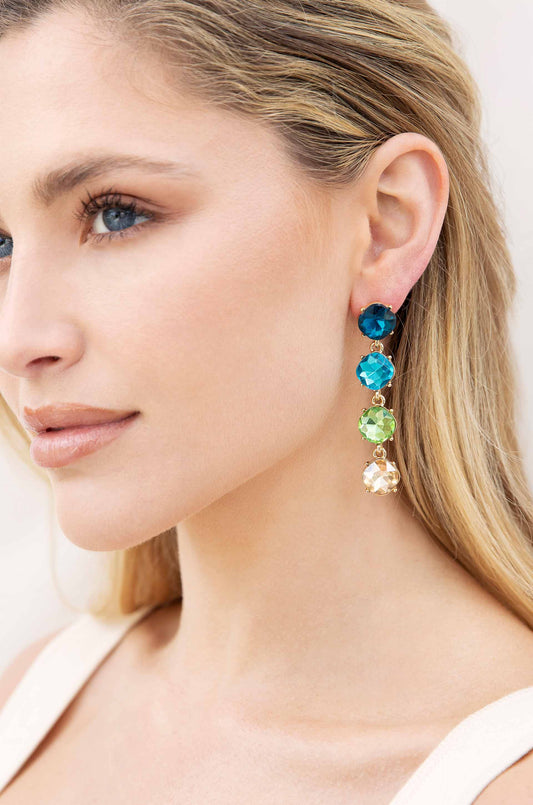 A woman's face is shown in profile, adorned with a colorful, multi-stone earring featuring shades of blue, green, and gold, set against a neutral background.