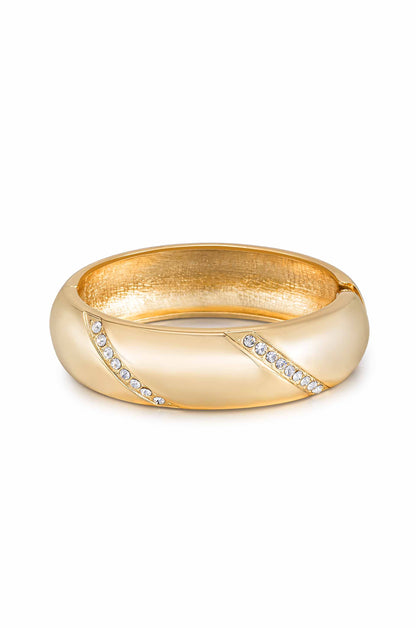 A golden ring with a smooth, shiny surface features a twist design, accented by small clear gemstones. It is positioned on a white background, highlighting its elegant appearance.