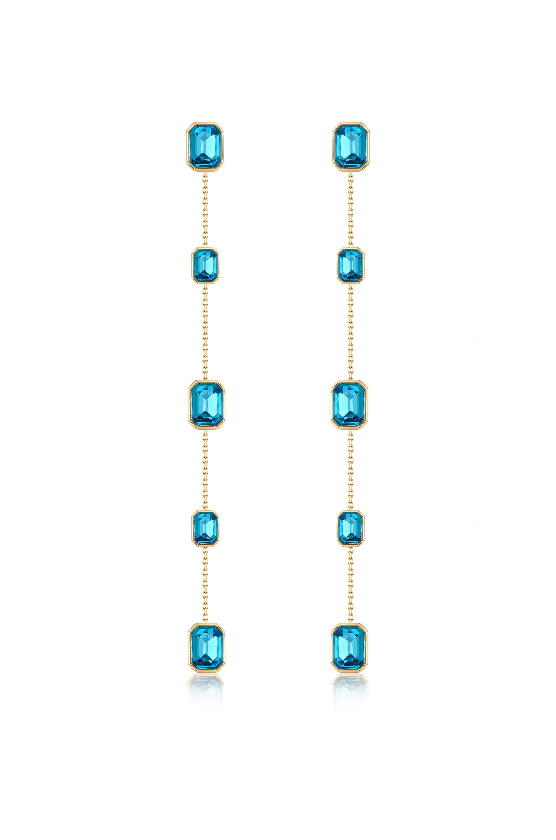 Dangling earrings feature a series of shimmering blue gems set in gold, elegantly hanging down in a vertical arrangement against a white background, highlighting their refined craftsmanship.