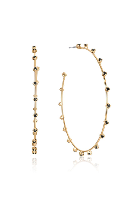 Gold hoop earrings adorned with small black stones are displayed side-by-side, reflecting light. The earrings feature a unique design with alternating shapes along the curve, emphasizing elegance.