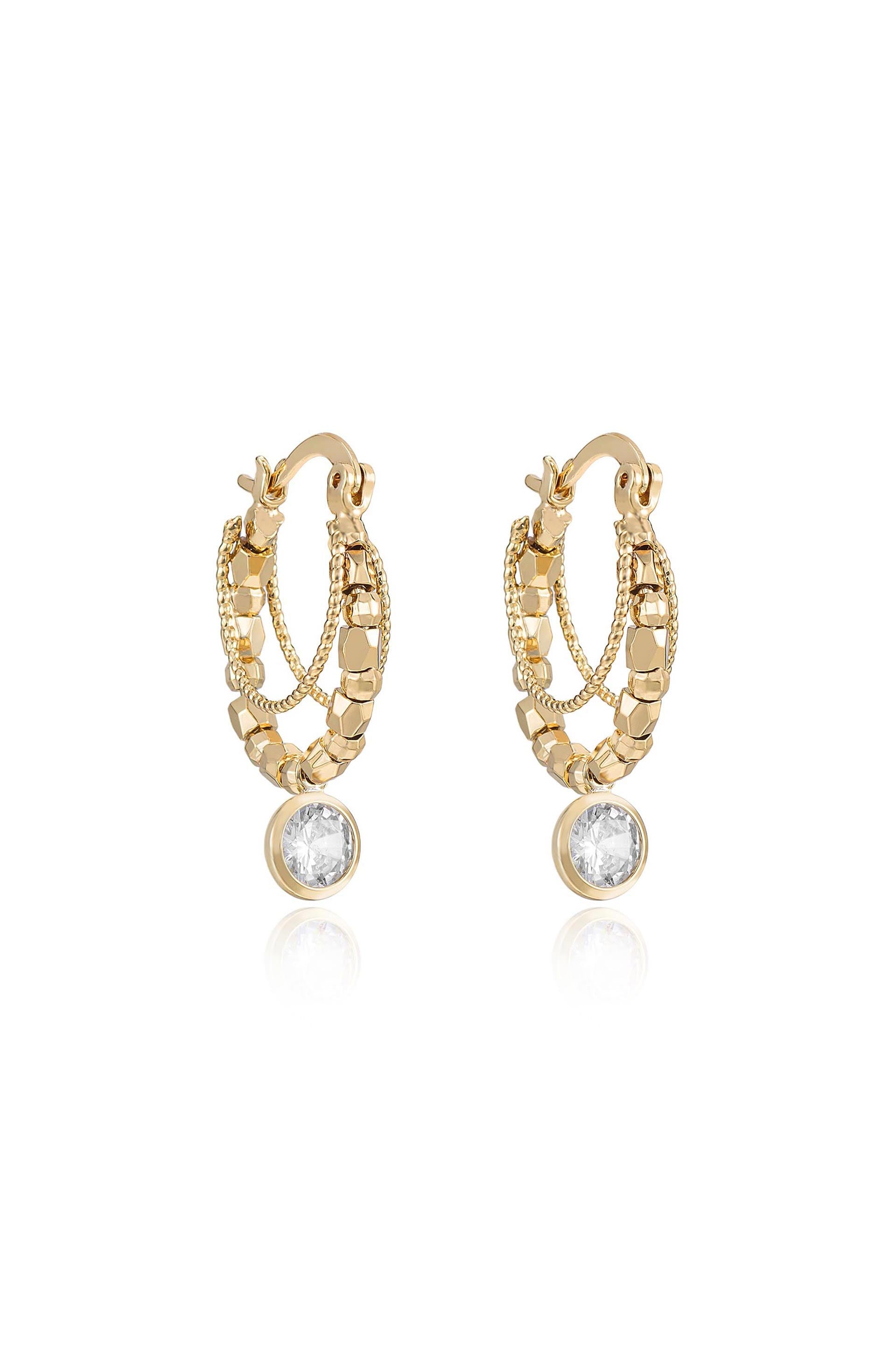 Gold hoop earrings feature intricate chain and bead detailing, with a single clear gemstone at the bottom, reflecting light, set against a neutral backdrop.