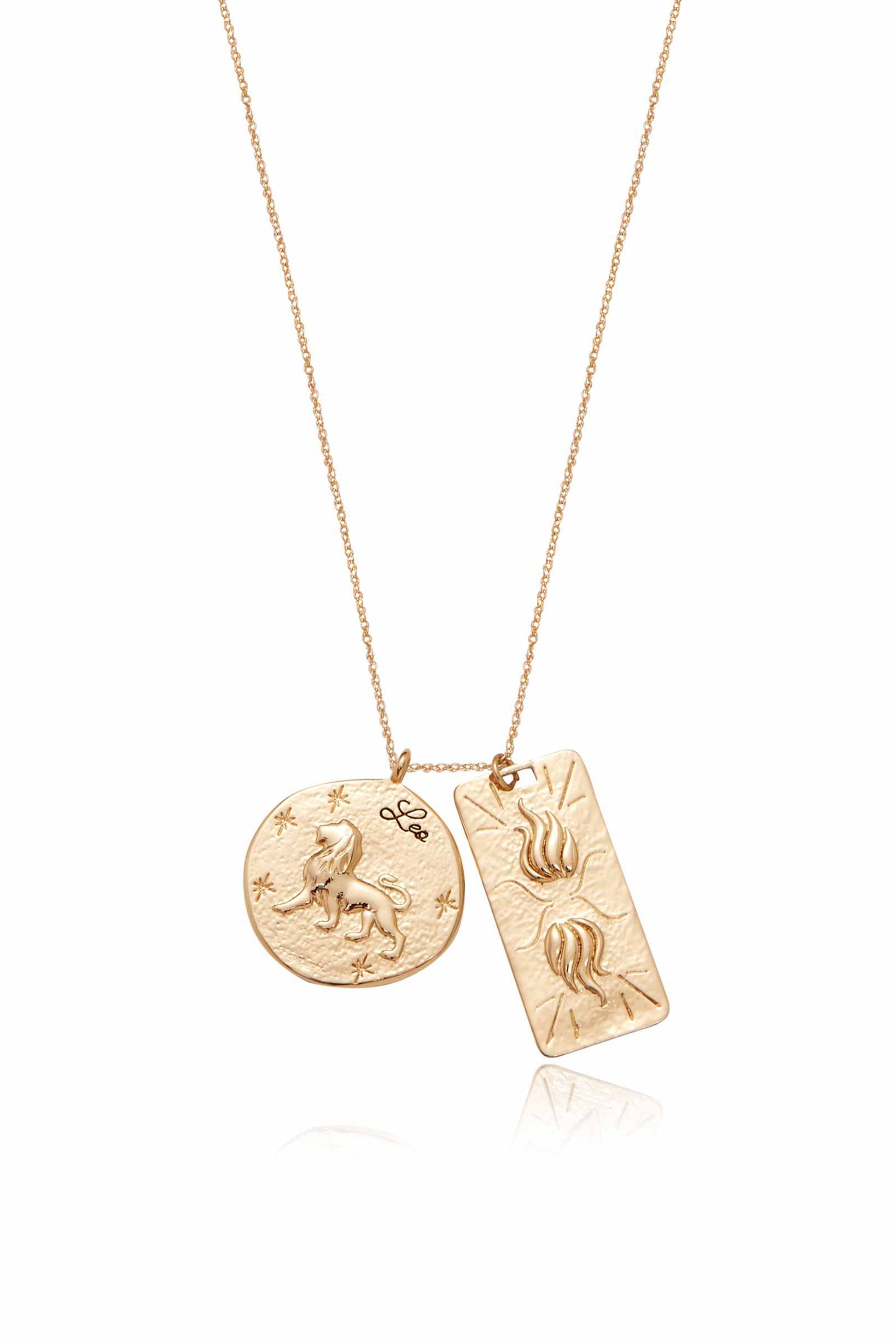 A gold necklace features two pendants: a round charm depicting a lion with â€œLeoâ€ inscribed, and a rectangular charm with flame-like designs. The background is plain white, emphasizing the jewelry.