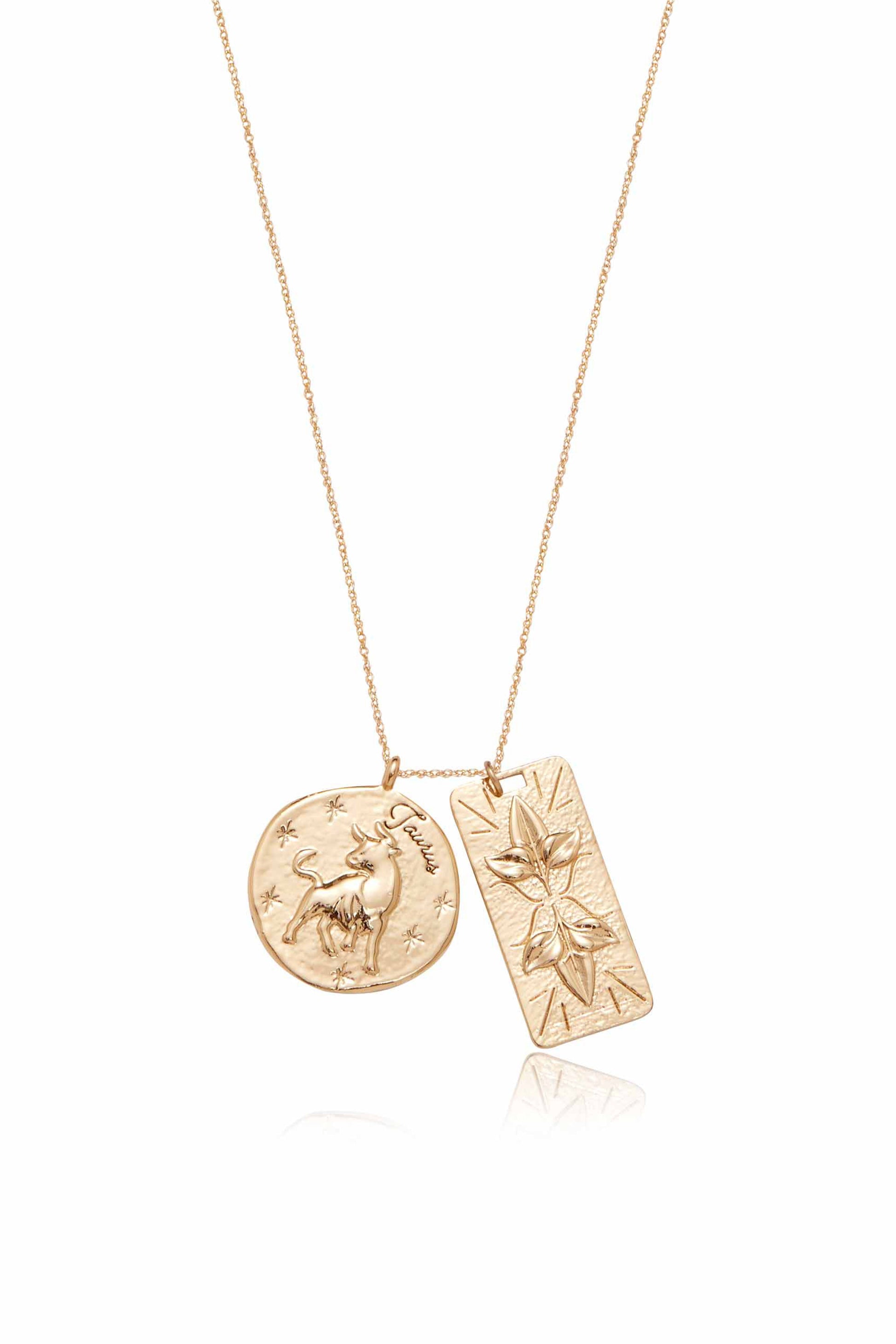 A gold necklace features two pendants: one circular with a bull design and "Taurus" inscribed, and a rectangular pendant with a floral engraving, set against a reflective surface.