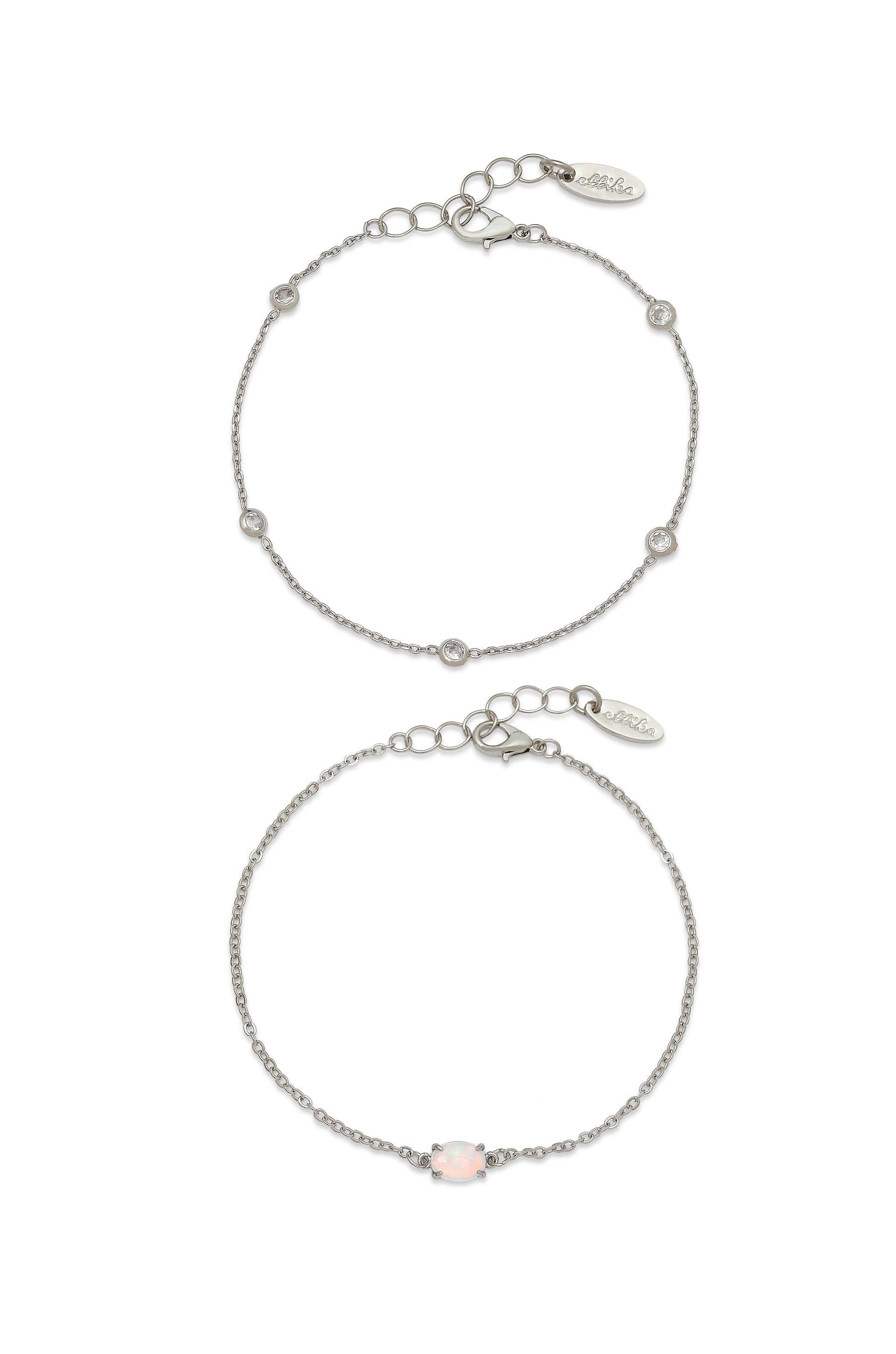 Two delicate silver bracelets, one adorned with small gemstones and the other featuring an opalescent stone, are clasped together, surrounded by a neutral background.