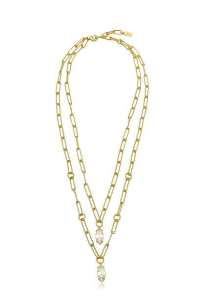 A gold layered necklace features elongated links and two sparkling crystal pendants hanging from the center, set against a plain white background. The design is elegant and modern.