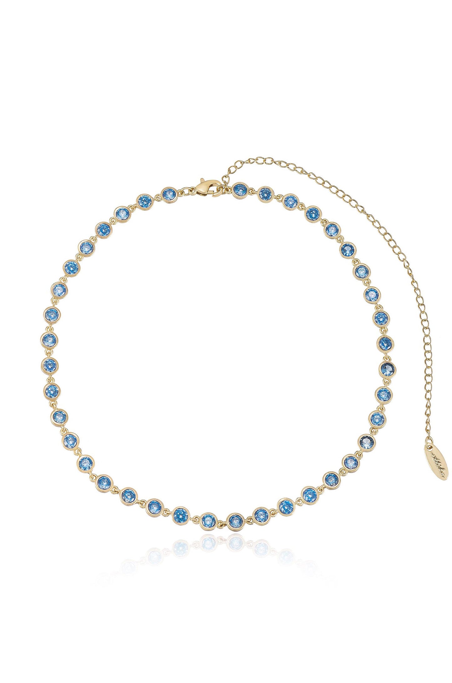 A gold necklace features a continuous line of blue gemstones, each set in a circular bezel. The piece is positioned against a white background, reflecting light off its surface.