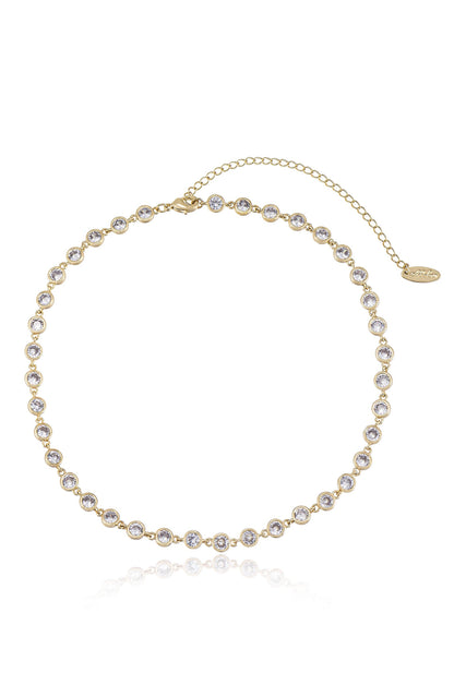 A gold choker necklace adorned with numerous sparkling stones is displayed against a reflective surface, showcasing its elegant design, ideal for formal occasions or enhancing everyday attire.