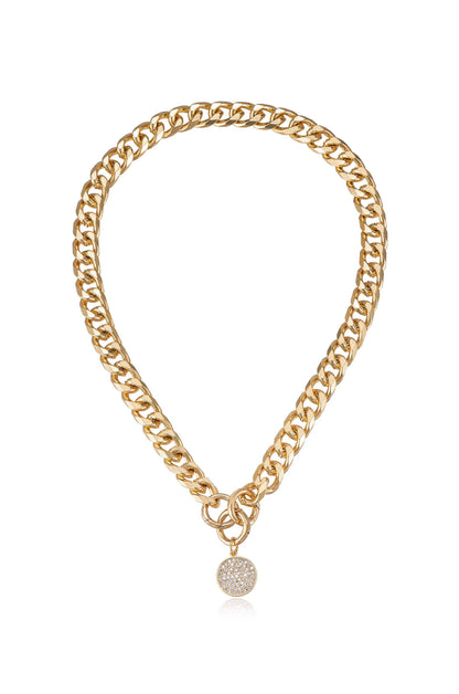 A gold chain necklace features thick, interlocking links with a circular charm adorned with small sparkling stones, suspended centrally. The background is simple, emphasizing the jewelryâ€™s shine and design.