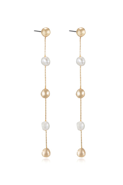 Two elegant earrings hang vertically, featuring alternating golden and white pearls on thin chains, set against a simple, light-colored background, emphasizing their delicate design.