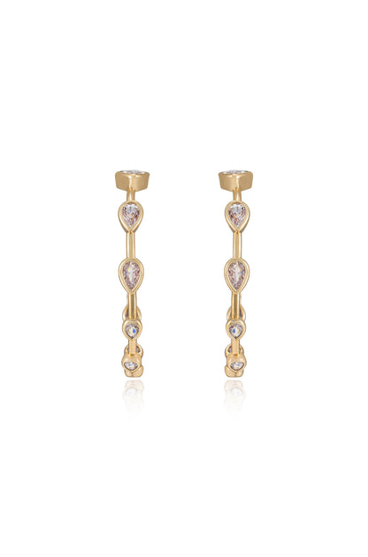 Two gold earrings feature a linear design adorned with teardrop and round stones. They are positioned upright against a reflective surface, showcasing their elegance and shine.