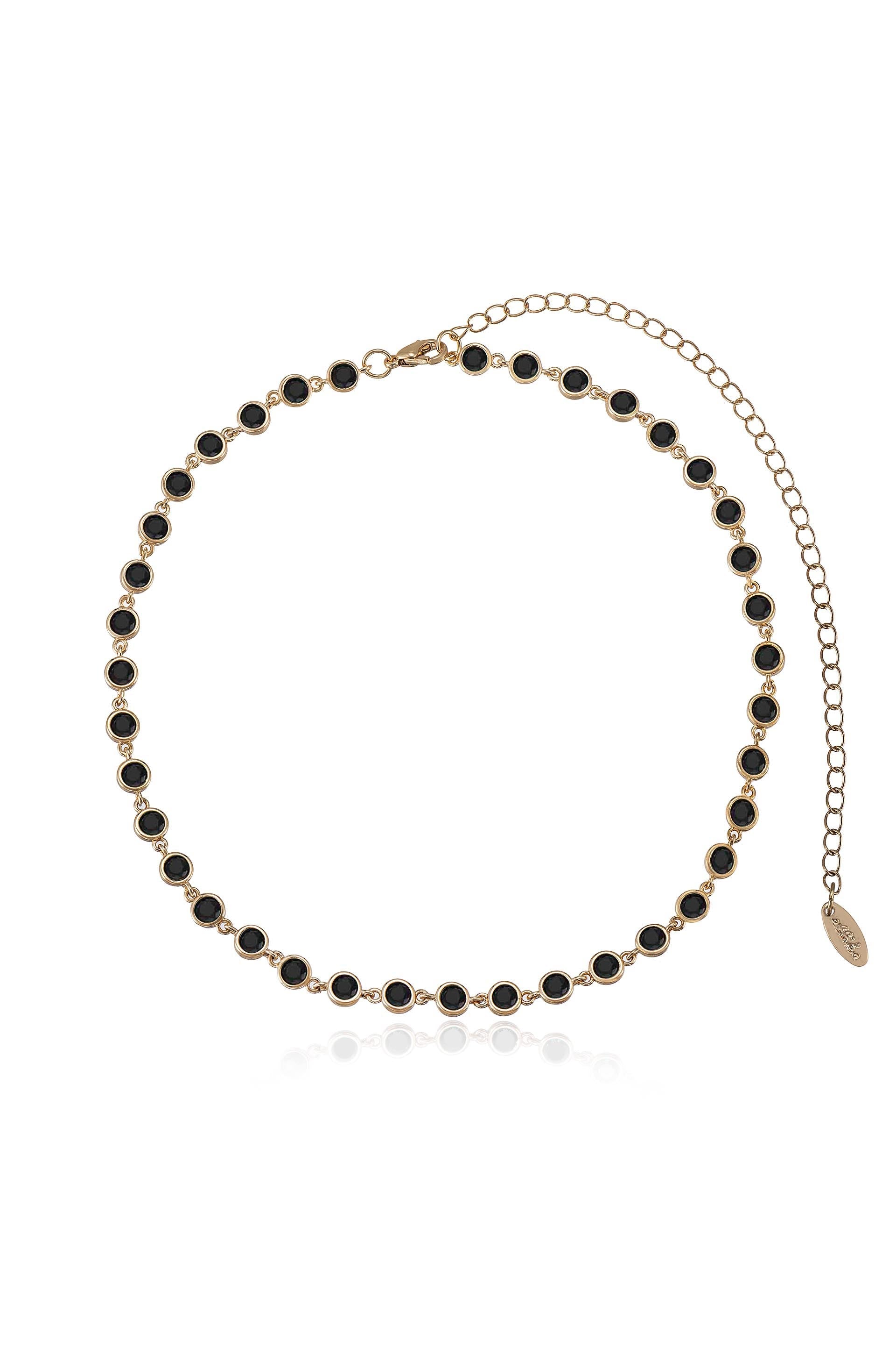 A gold-toned necklace features a series of evenly spaced black circular stones, creating a polished appearance. It is displayed against a white background, highlighting its elegant design.