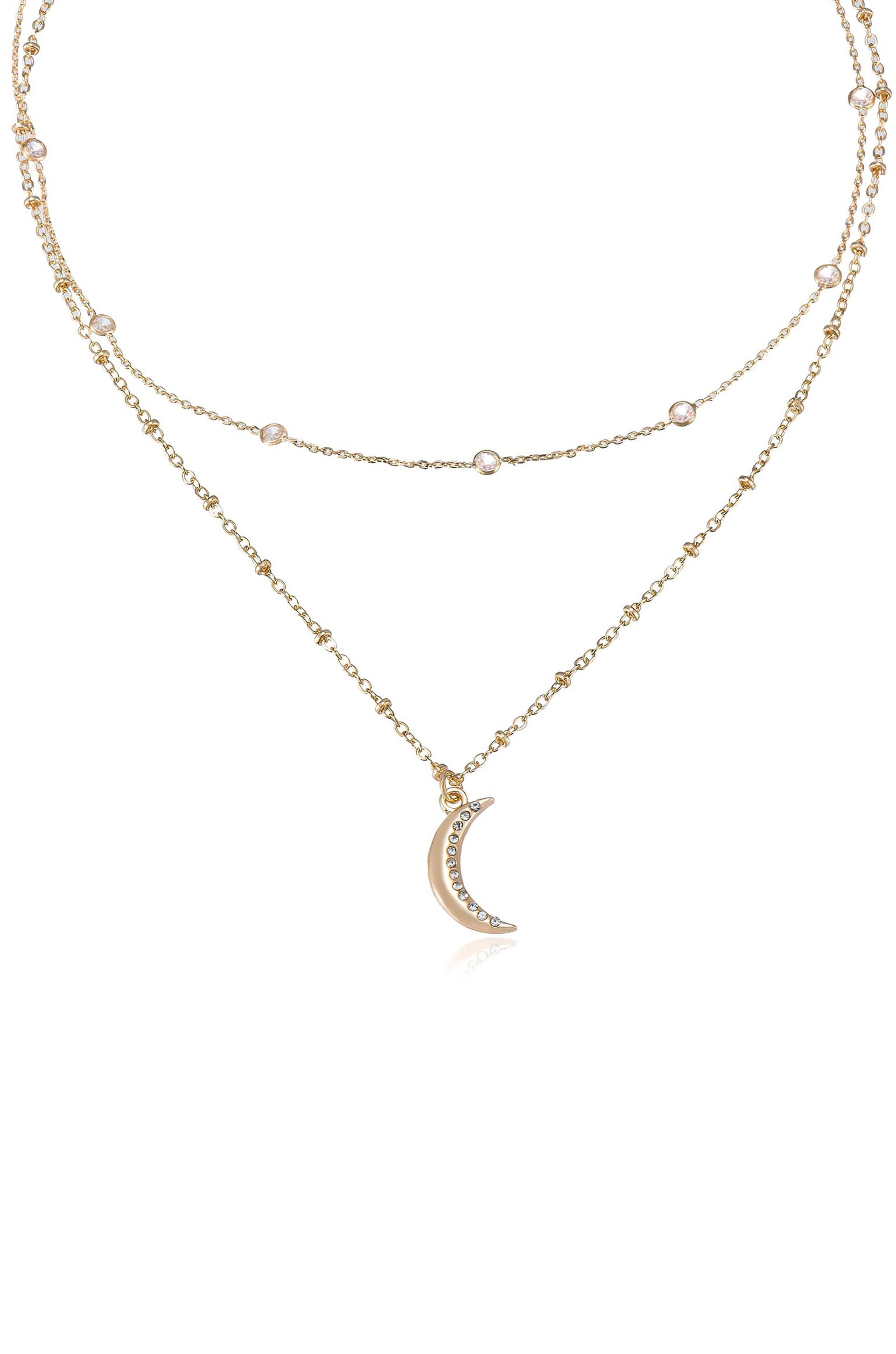 A gold necklace features two delicate chains with small round beads, anchored by a crescent moon pendant adorned with sparkling rhinestones, set against a plain white background.