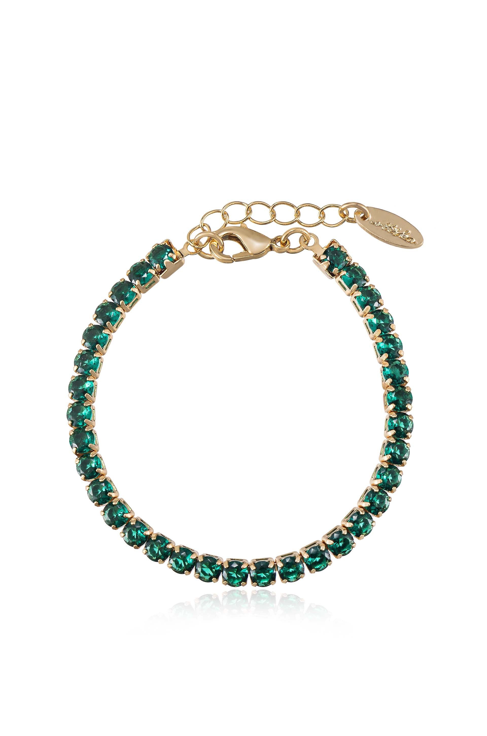 A gold bracelet adorned with green gemstones is displayed, resting against a reflective surface. The clasp and extension chain suggest it is designed for adjustable fitting and secure wear.