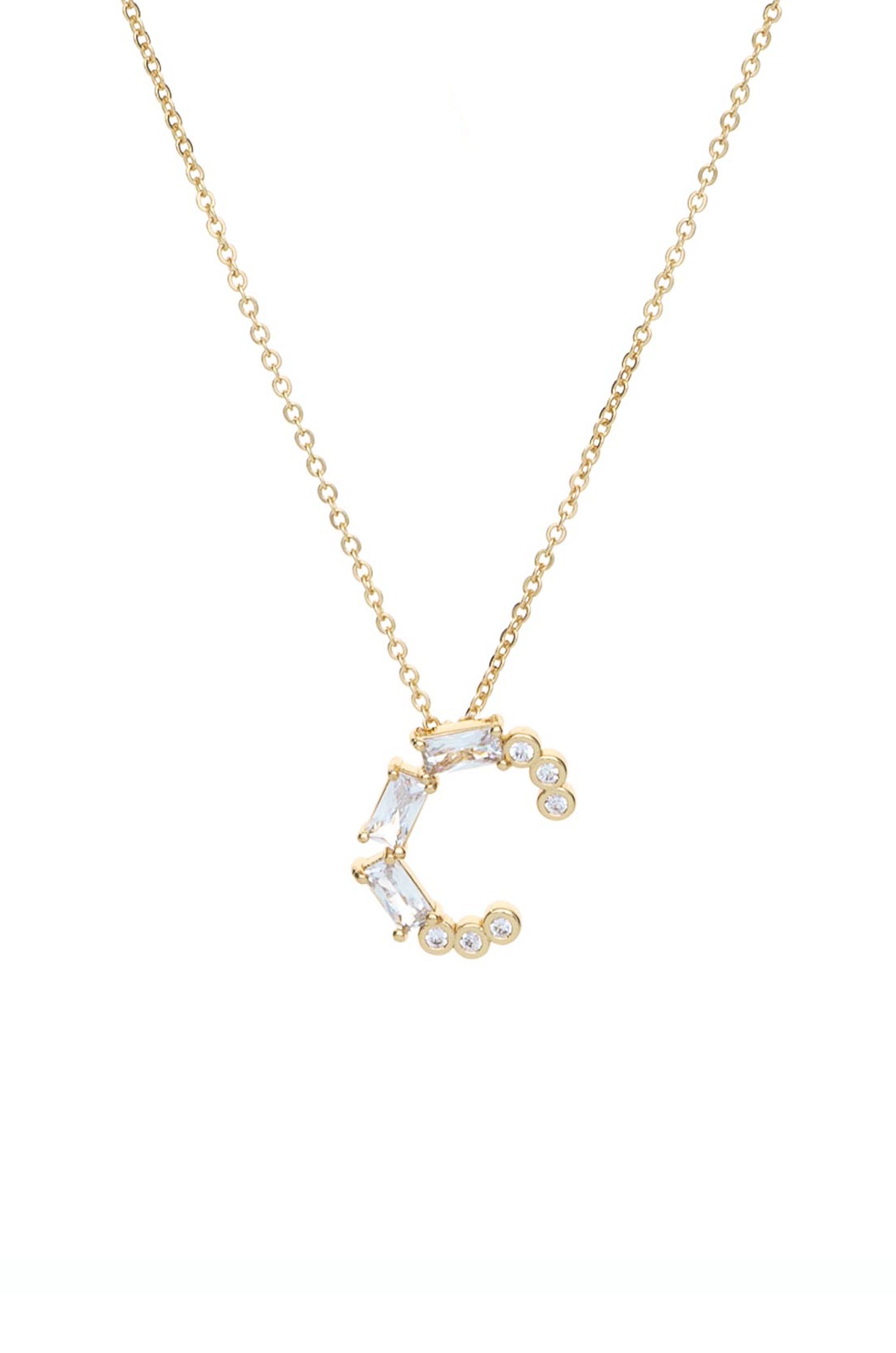 A gold necklace features a delicate pendant shaped like the letter "C," adorned with clear gemstones and arranged in a stylish, contemporary design against a plain white background.