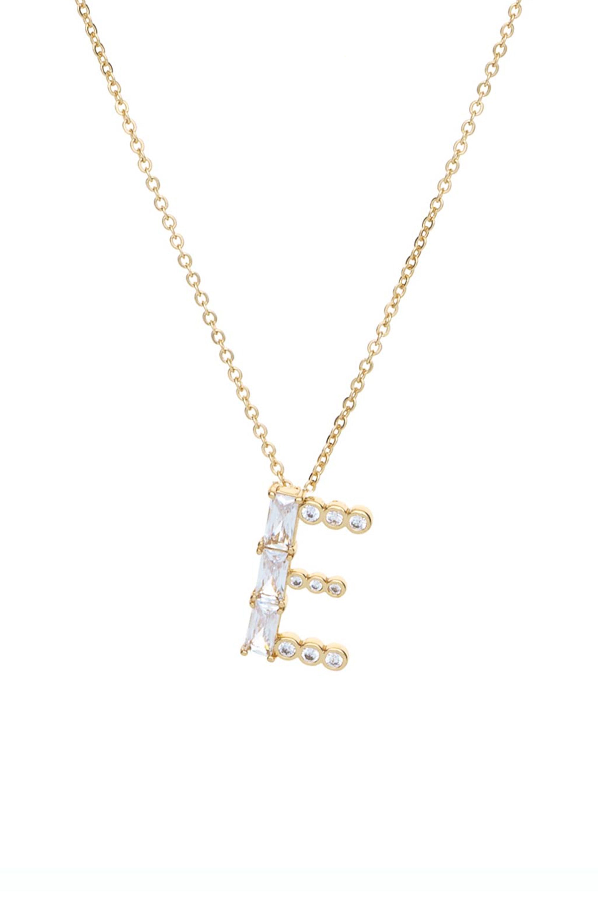 A golden necklace features a stylized letter "E" adorned with sparkling gemstones. It hangs against a plain white background, highlighting its elegant design.