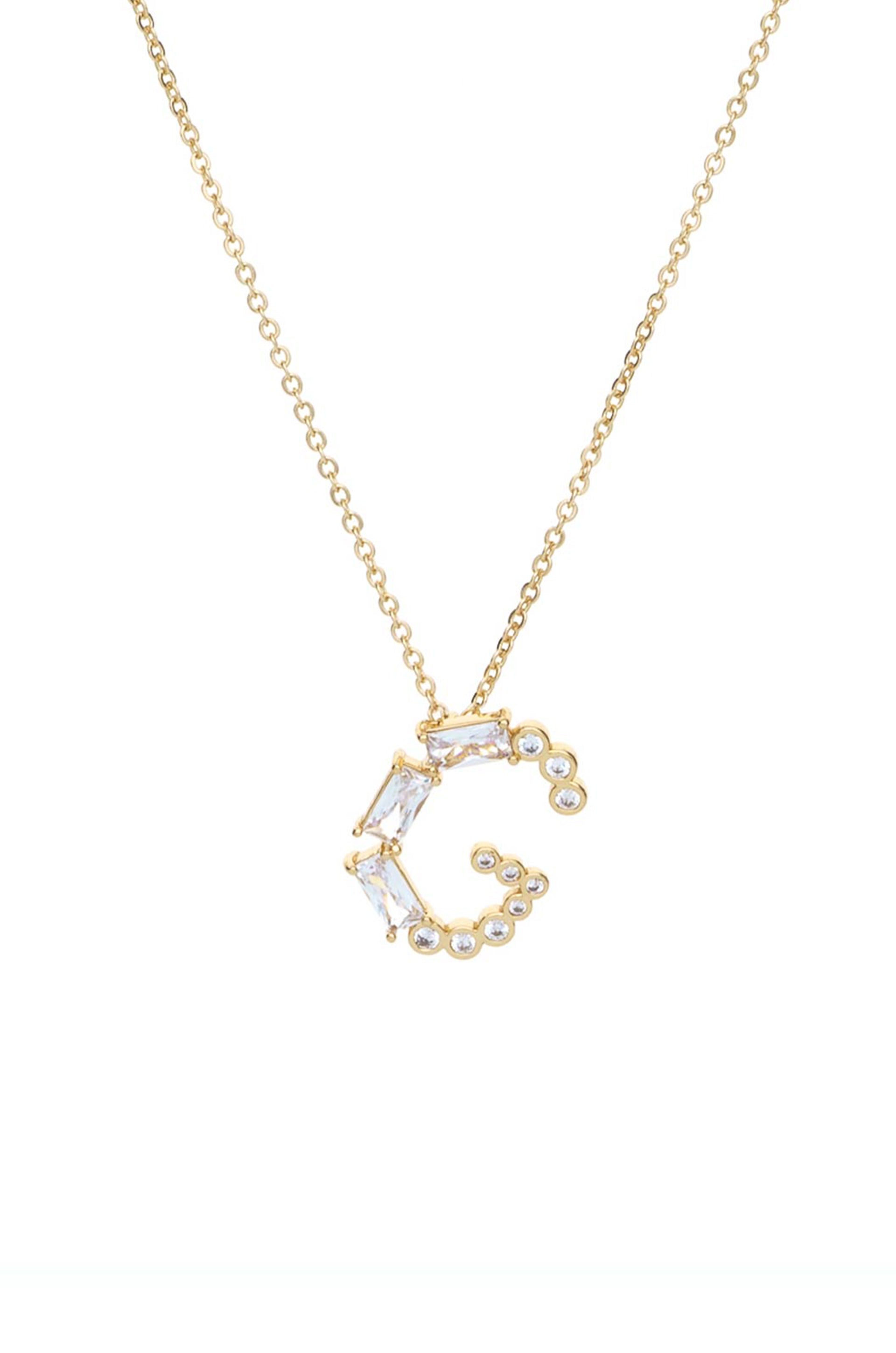 A gold necklace features a decorative pendant shaped like the letter "C," adorned with rectangular and round clear stones, against a plain white background.