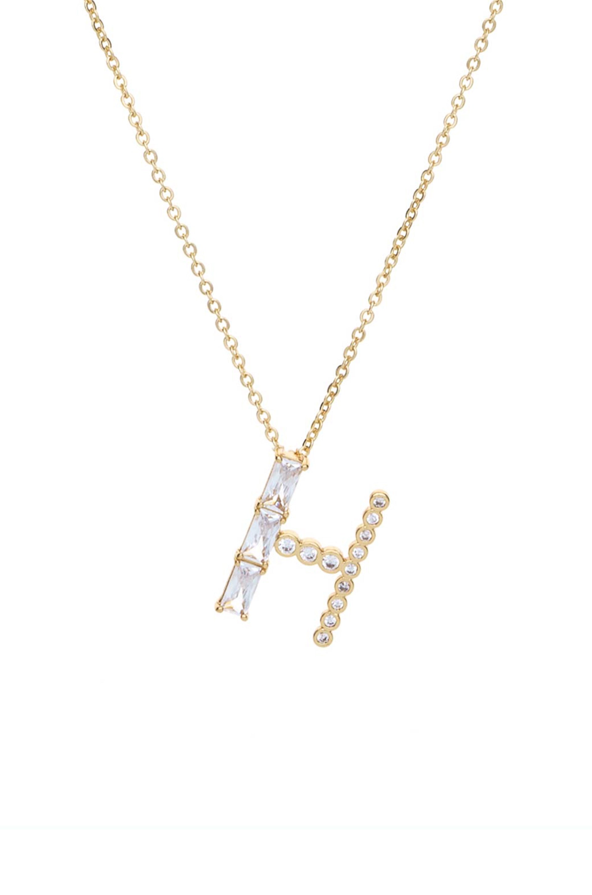 A gold necklace features a prominent, stylized letter "H" adorned with sparkling gemstones. The chain is delicate, set against a plain white background, highlighting its elegance.