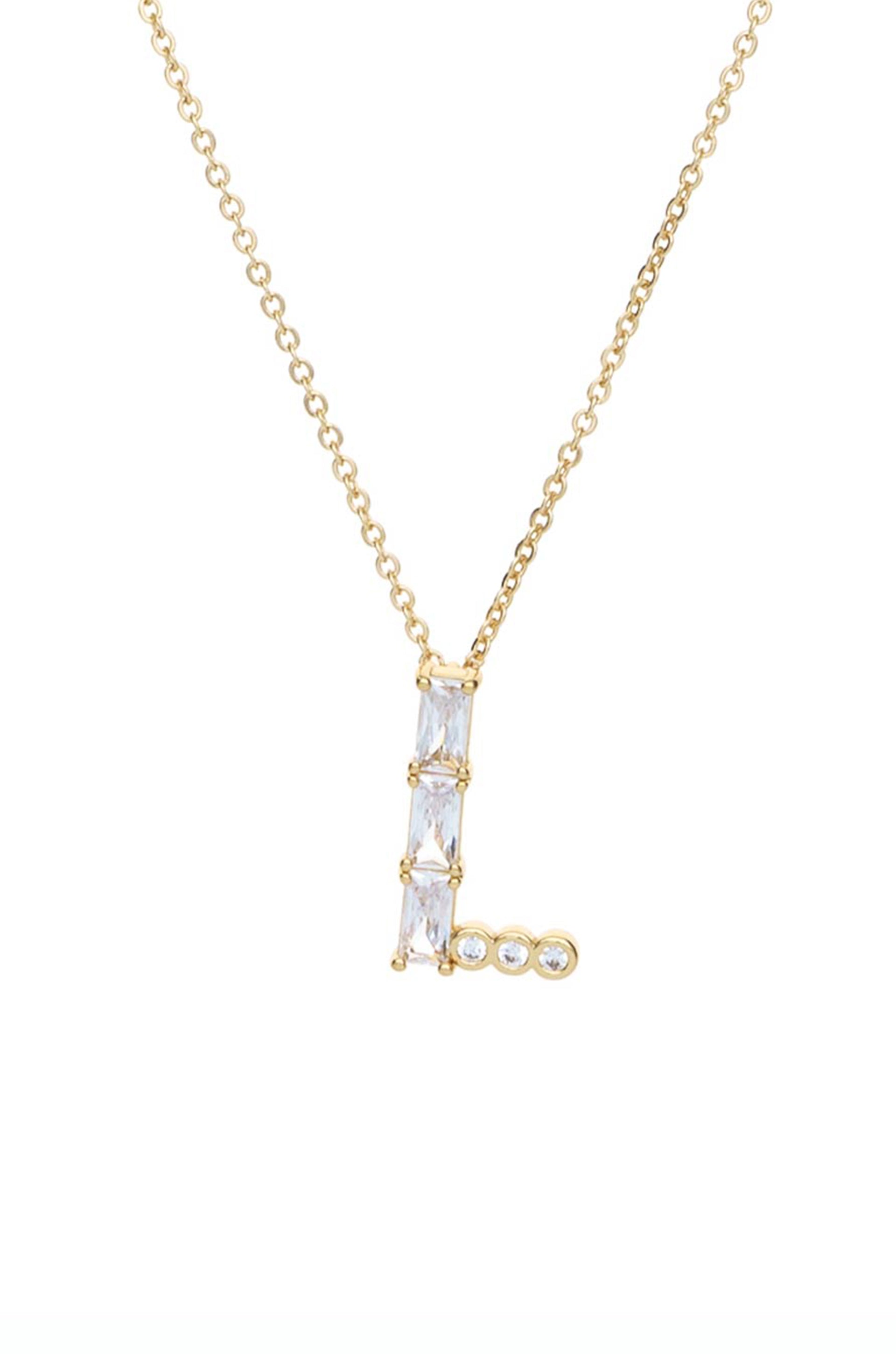 A gold necklace features a pendant shaped like the letter "L," adorned with multiple clear stones, showcasing an elegant design against a white background.