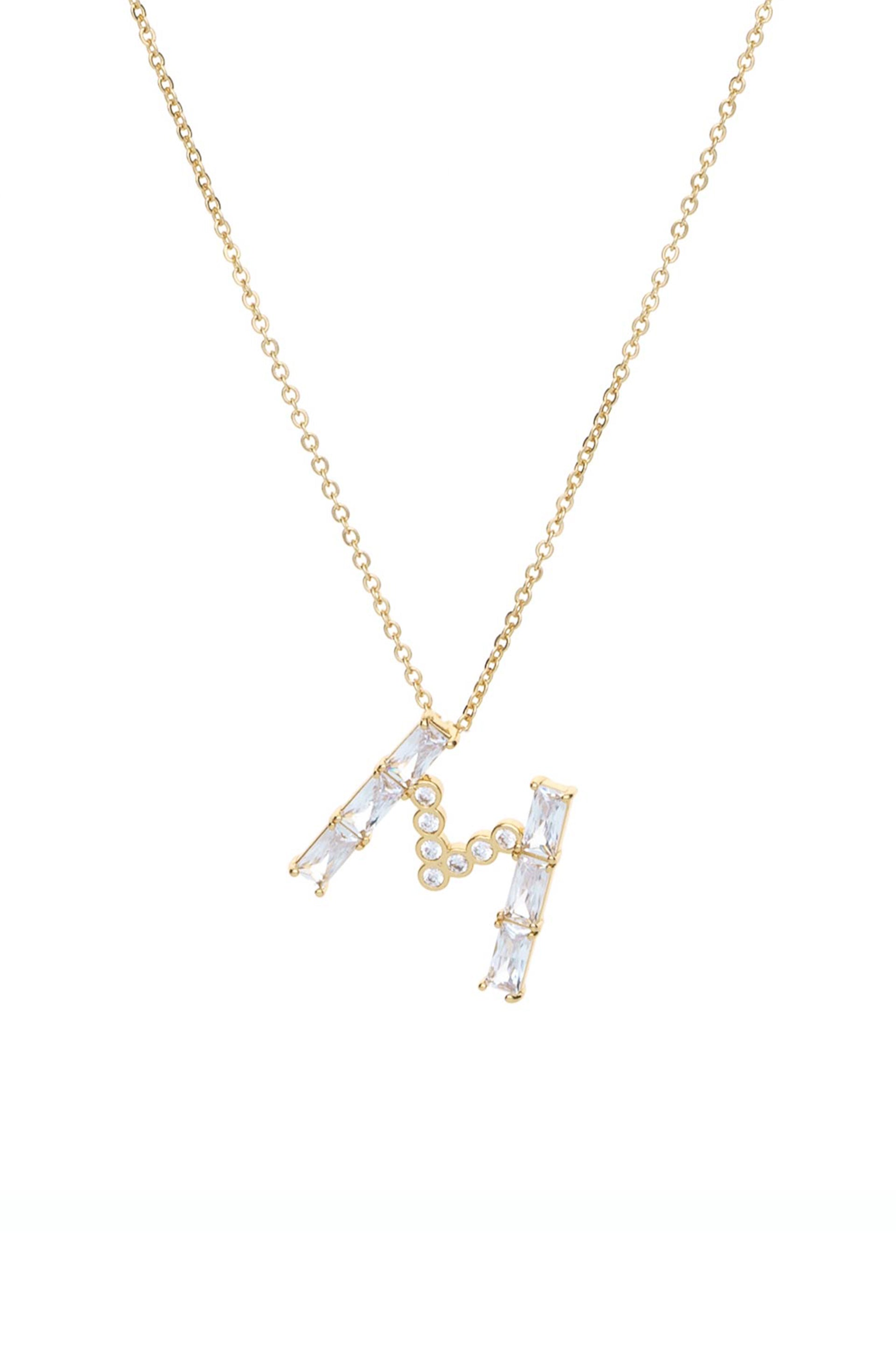 A gold necklace features a decorative letter "M," embellished with rectangular and circular diamonds, suspended from a delicate chain against a plain white background.