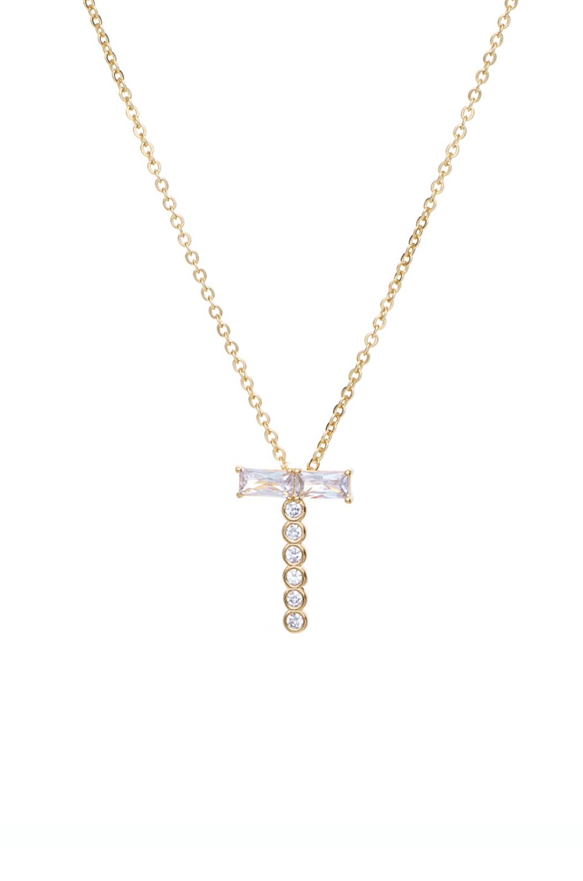 A gold chain necklace features a cross pendant adorned with a central rectangular gemstone and a vertical row of round gemstones, all set against a plain white background.