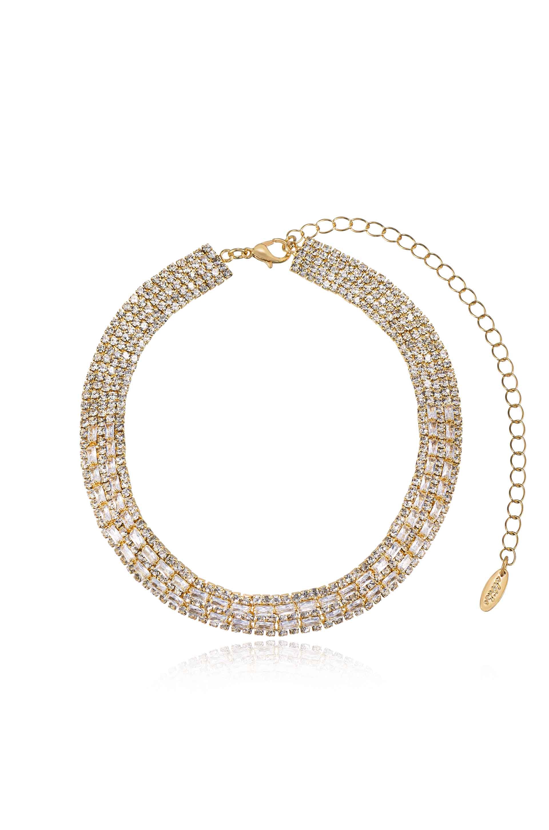 A gold-toned necklace adorned with glittering stones glimmers softly. It is clasped at one end, and a chain extension is included, allowing for adjustable fit. The background is plain.