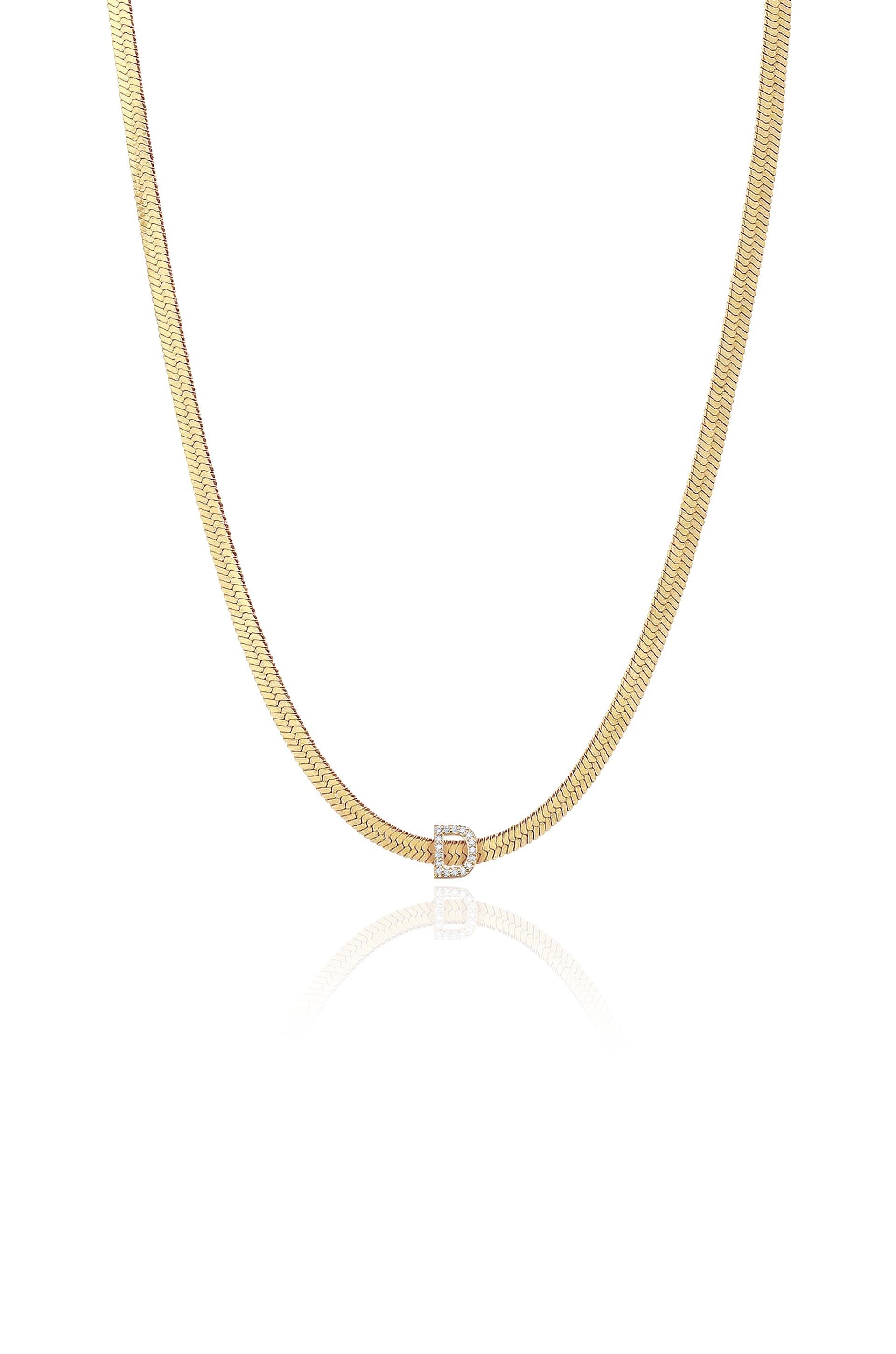 A gold chain necklace is displayed, featuring a central clasp with a diamond-encrusted "D." The reflective surface subtly highlights the necklace against a white background.