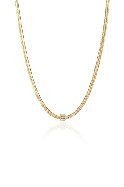 A gold chain necklace is displayed, featuring a central clasp with a diamond-encrusted "D." The reflective surface subtly highlights the necklace against a white background.