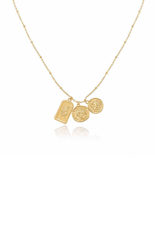 A golden necklace features three decorative charms, including two medallions and one rectangular piece, all hanging from a delicate chain against a plain white background.