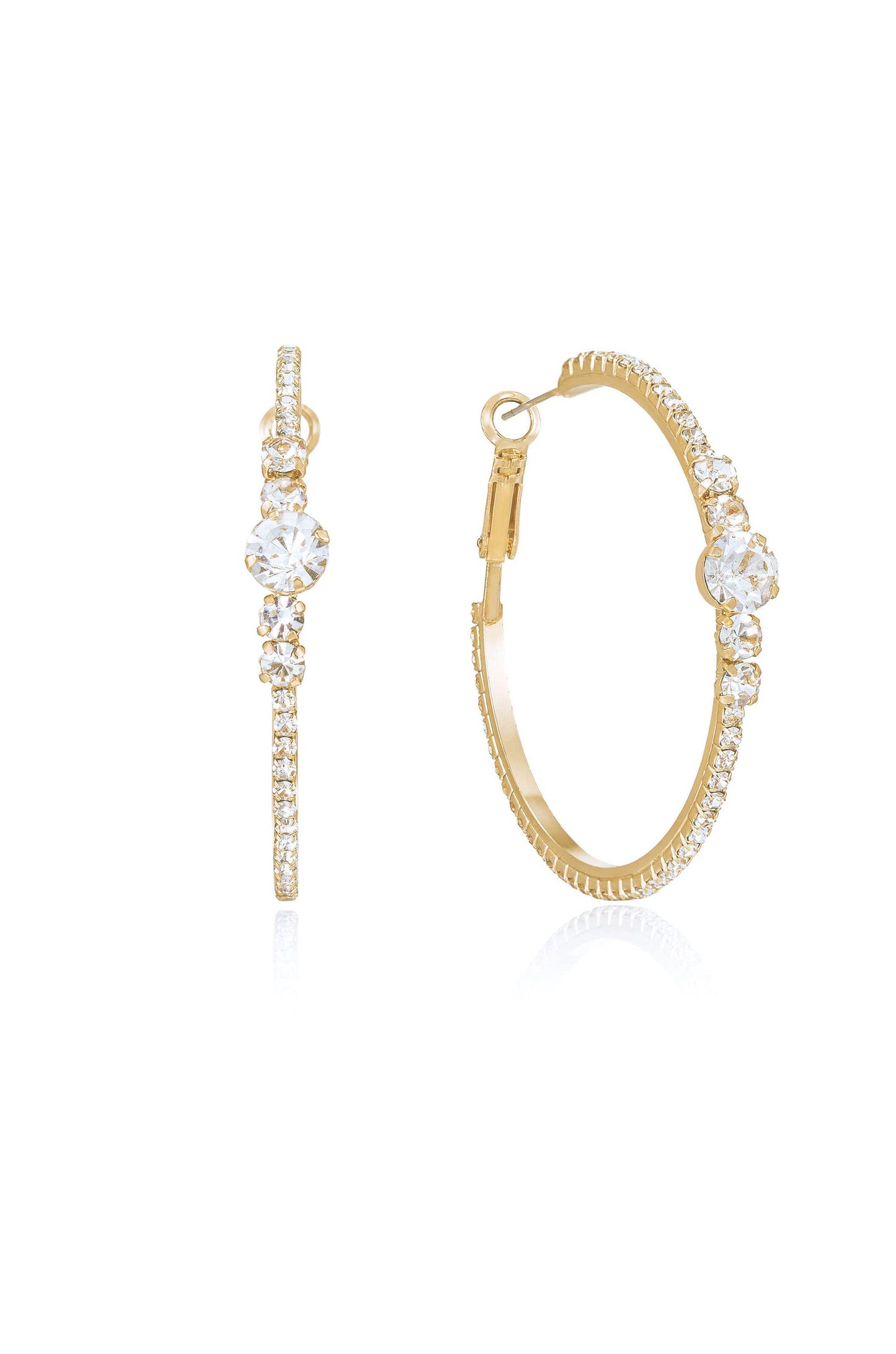 Gold hoop earrings adorned with sparkling clear gemstones are positioned upright against a white background, showcasing their shiny surface and intricate design details.