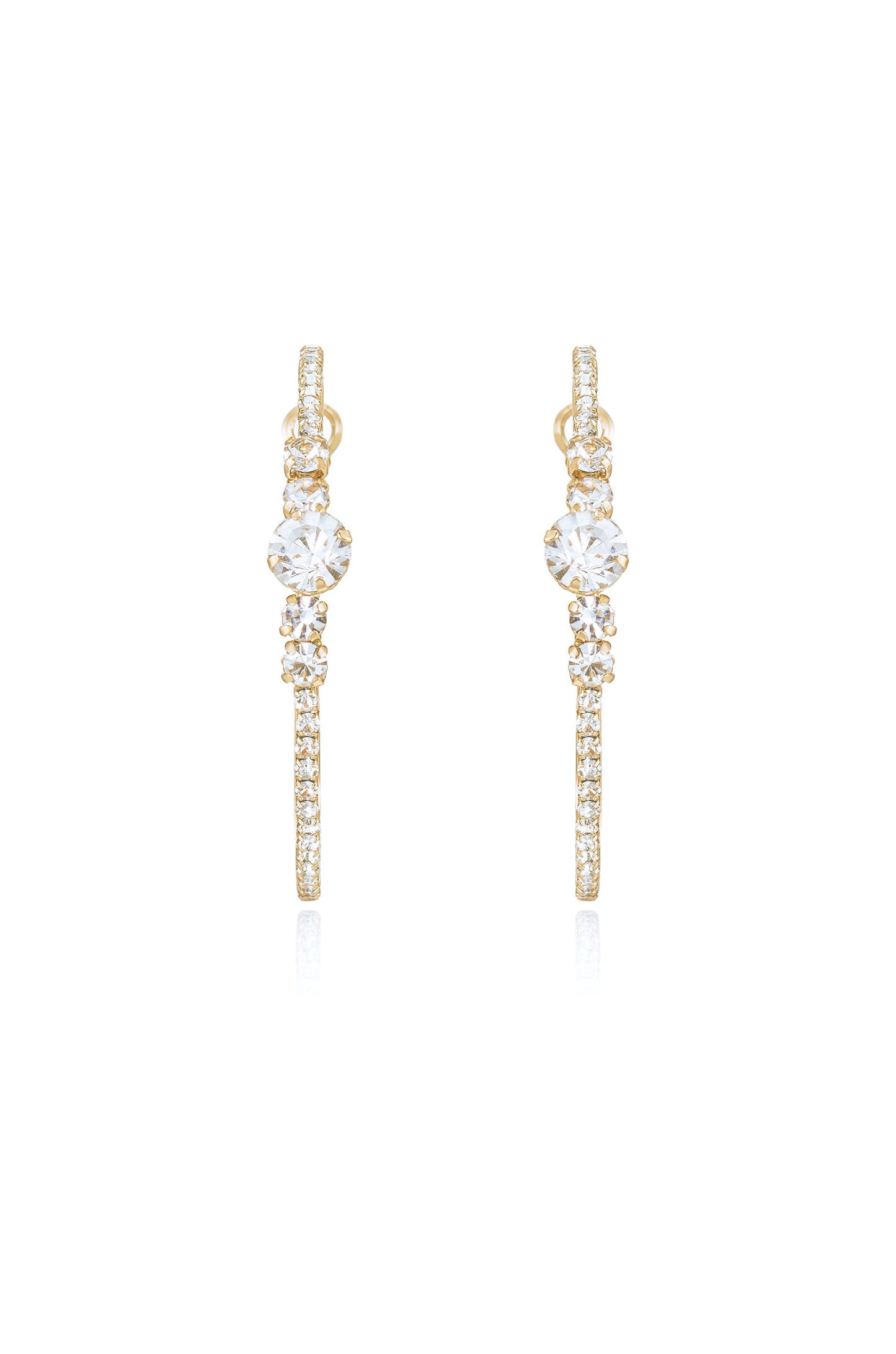 Gold earrings adorned with sparkling crystals hang vertically, catching light and reflecting it. They are displayed against a white background, emphasizing their elegance and shine.