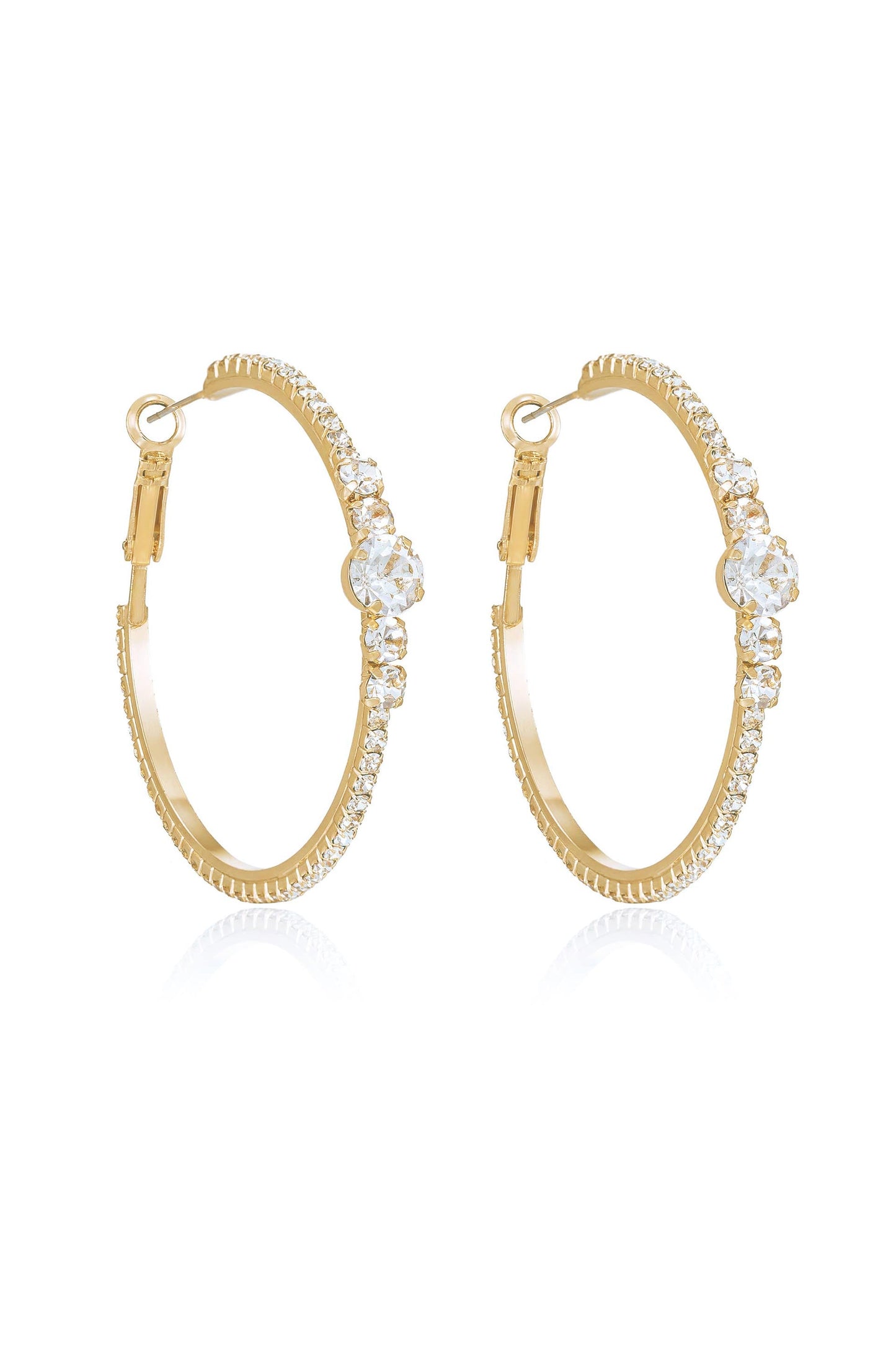 A pair of gold hoop earrings with sparkling clear stones along the outer edge and a larger stone prominently featured at the center, set against a reflective white background.