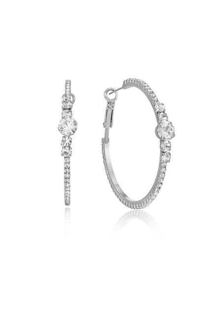 A pair of elegant silver hoop earrings is displayed, featuring multiple embedded clear gemstones. They are positioned against a plain white background, emphasizing their sparkle and design.