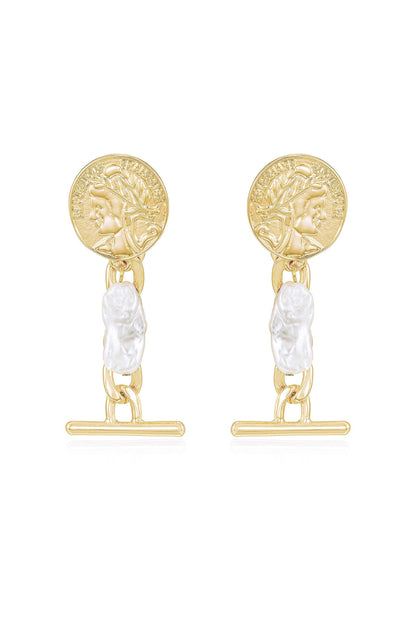 Gold-colored earrings feature a round coin with a profile design, linked by a chain to a carved white pearl-like piece. They are displayed against a neutral background.