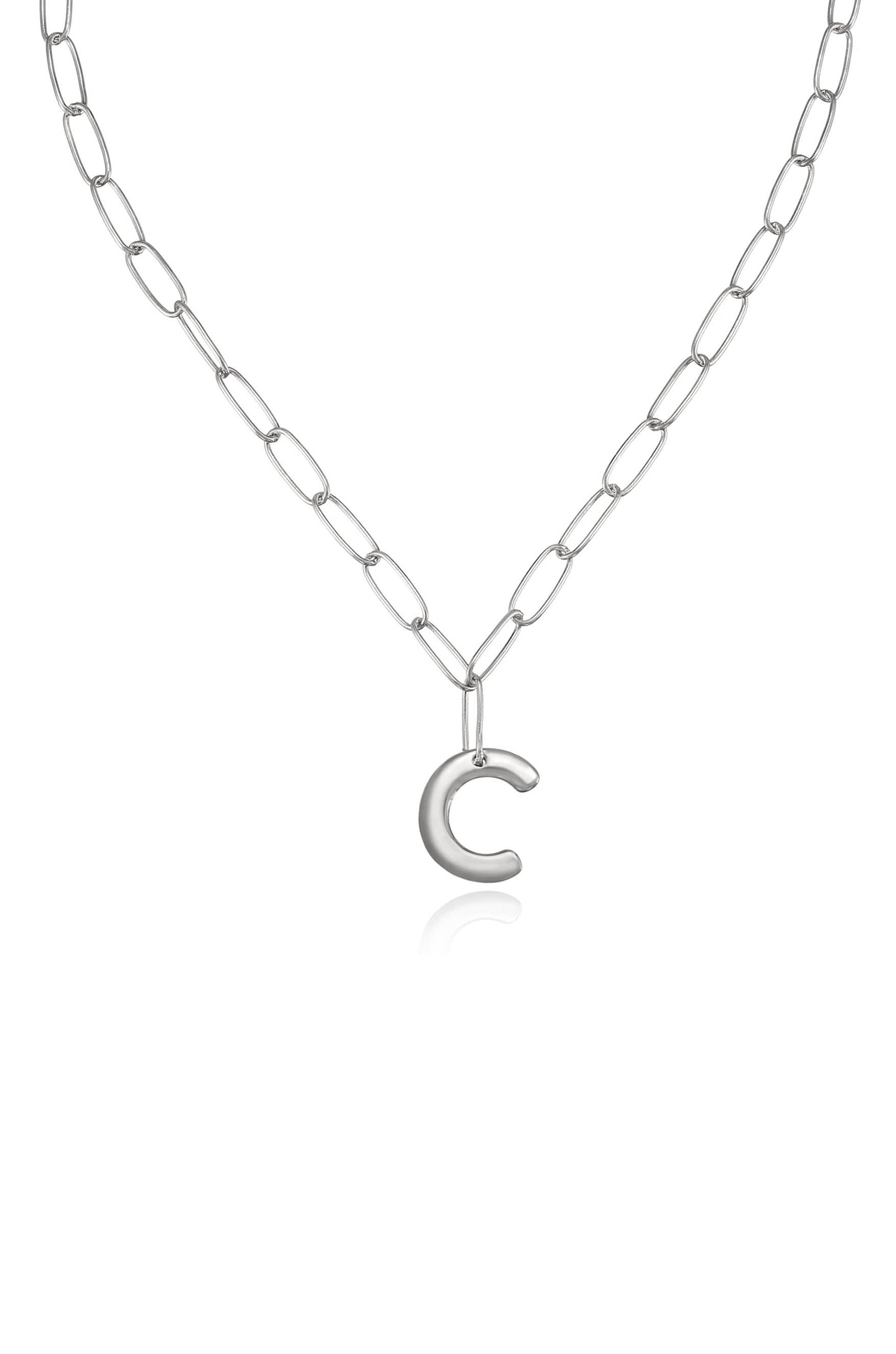 A silver chain necklace features elongated links and a shiny, stylized letter "C" pendant hanging from it. The background is neutral, emphasizing the jewelry's design.