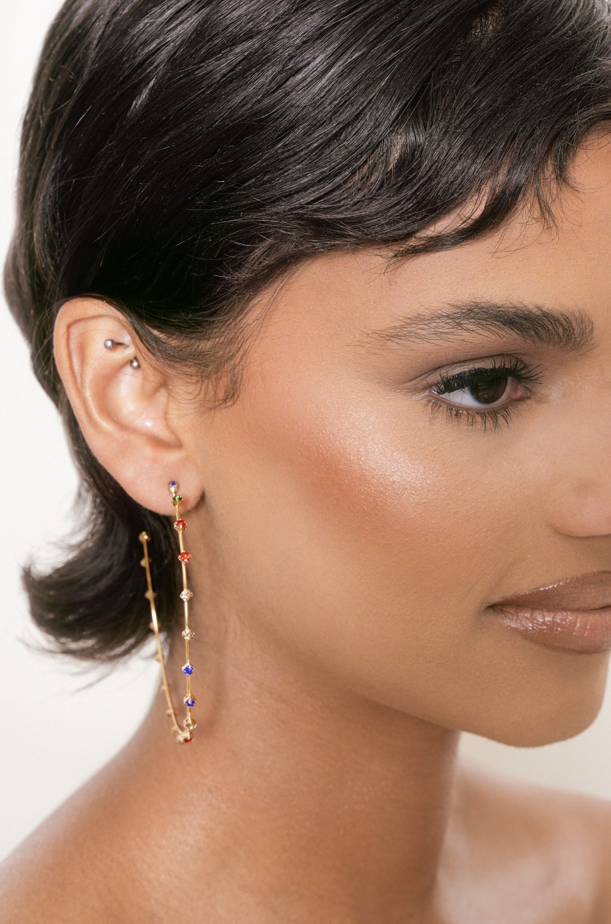 A close-up of a personâ€™s face showcases a sleek bob hairstyle. A long, decorative earring with colorful beads hangs from their ear, set against a neutral background.