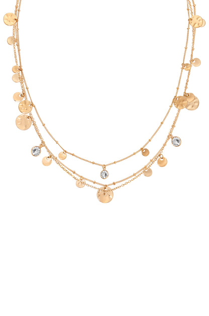 A layered gold necklace with circular pendants and sparkling gemstones glimmers against a plain white background, showcasing its design and elegance.