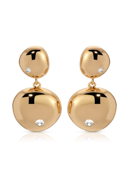 Two gold earrings dangle elegantly, featuring polished, rounded shapes adorned with small, sparkling diamonds. They rest on a white surface, reflecting light and enhancing their luxurious appearance.