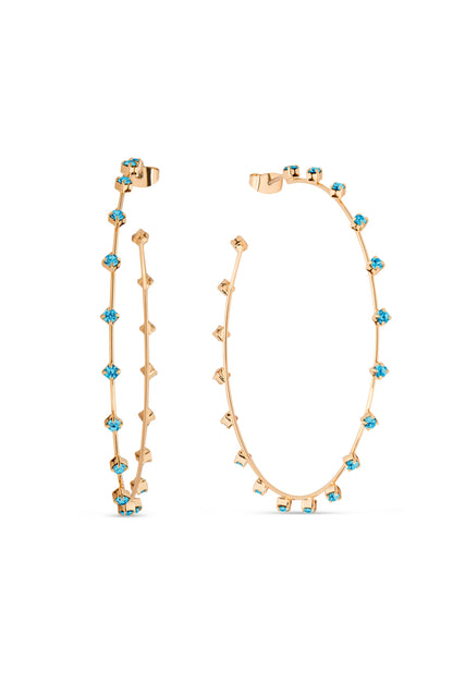 Two gold hoop earrings stand side by side, embellished with blue gemstones. Their slender design features alternating shapes and colors, showcasing elegance against a plain white background.