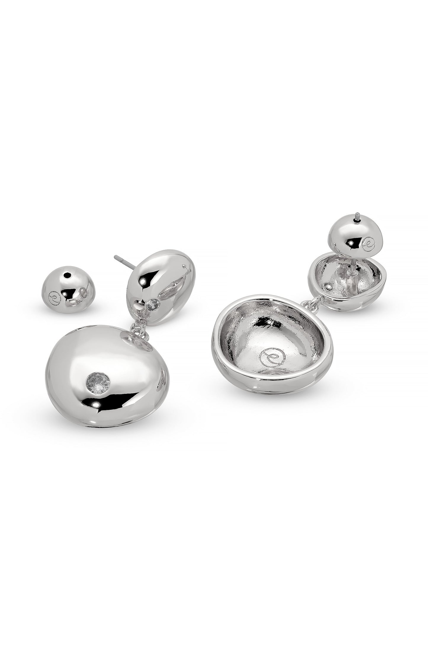 Two pairs of silver earrings are displayed. One features a solid disc with a small diamond, while the other has a hollow, oval shape with a shiny interior, showcasing their unique design.