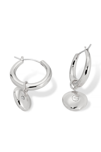 Silver hoop earrings are displayed, featuring a shiny, smooth design with a circular charm attached. The earrings are set against a plain white background, emphasizing their reflective surface.