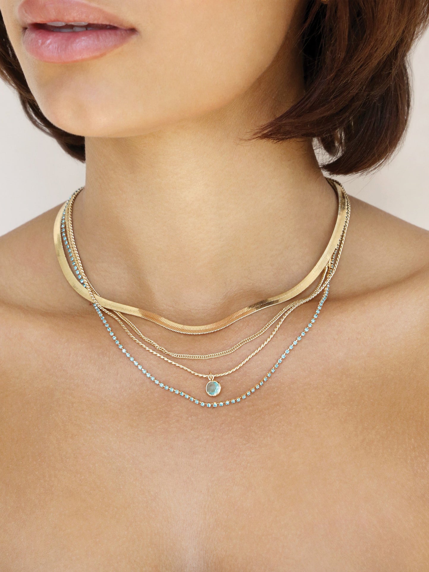 A close-up of a neck adorned with multiple gold and silver necklaces, resting elegantly against smooth skin, enhancing the simplicity and beauty of the individual's collarbone and neckline.