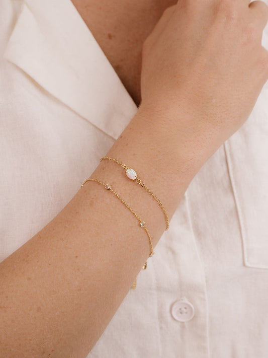 A hand with several delicate gold bracelets rests against a light-colored fabric, showcasing the jewelryâ€™s shimmer against the skin, emphasizing elegance and simplicity in style.